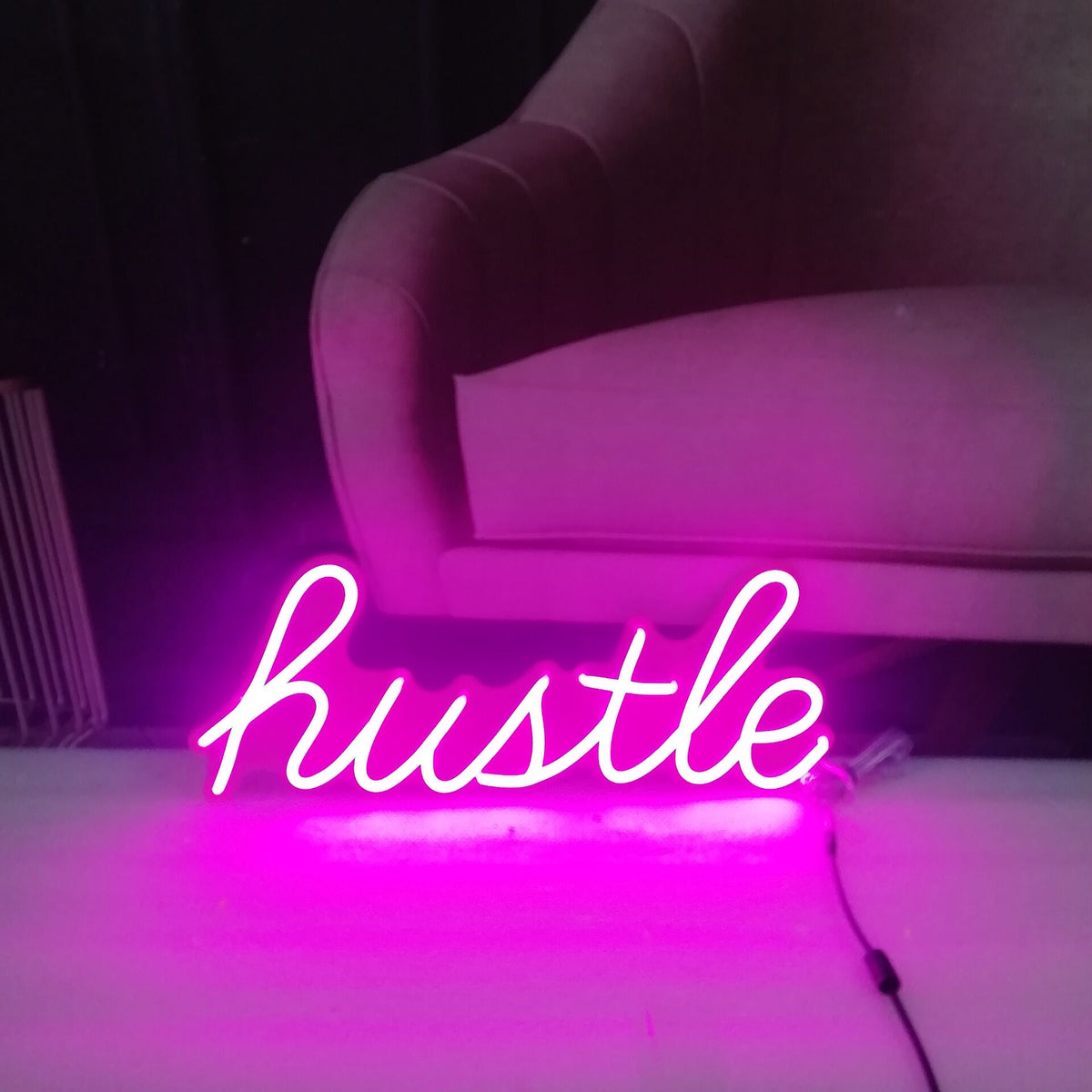 Pink Hustle script LED neon sign displayed beside a chair