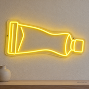 Watermarked concept mockup of Mini Paint Tube LED Neon Sign in Yellow on a clear acrylic backboard.