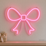 Watermarked concept mockup of the Mini Ribbon Bow LED Neon Sign in Pink on a clear acrylic backboard.